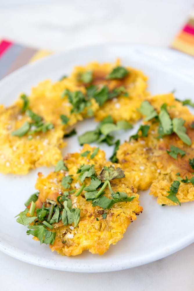 Tostones (patacones or twice fried green plantains) on a plate, topped with cilantro