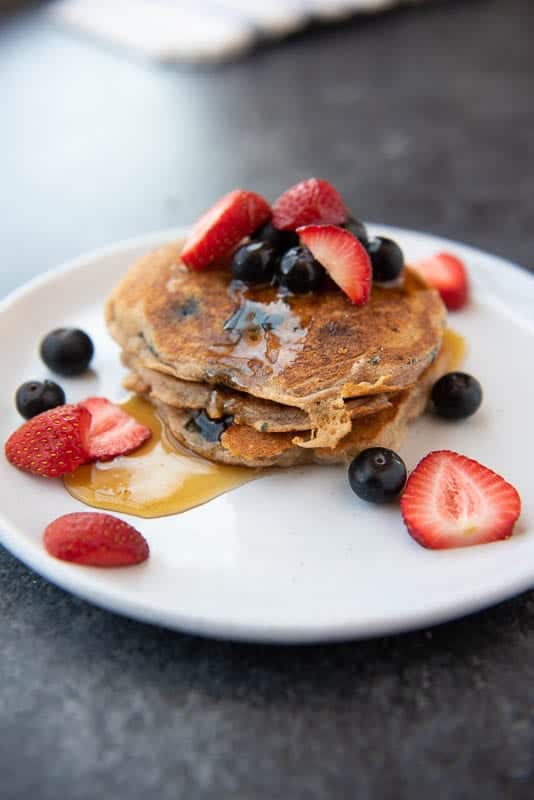 AIP Cassava Flour Pancakes on a plate, drizzled with maple syrup and topped with fresh berries