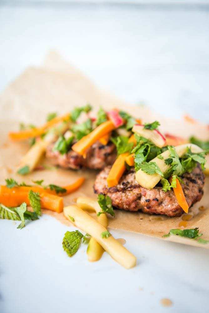 A side view of the Paleo AIP Banh Mi Burger on parchment paper with the pickled toppings