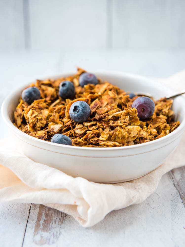 Pumpkin granola from the side in a bowl topped with blueberries