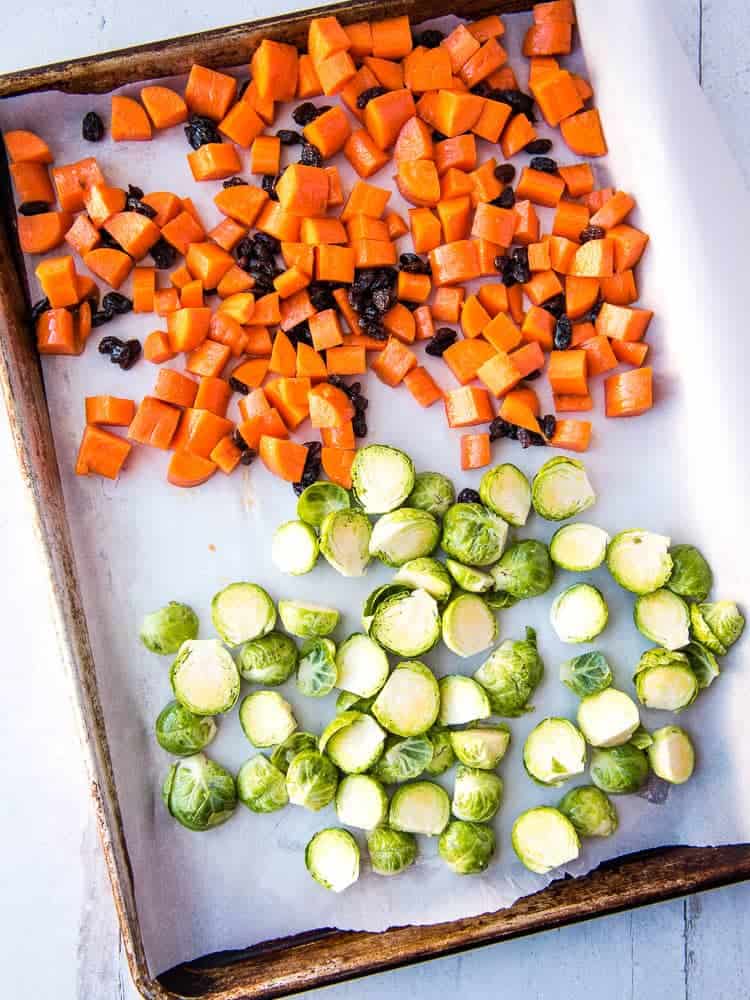 candied carrots and raisins and brussels sprouts on a baking sheet covered with parchment paper