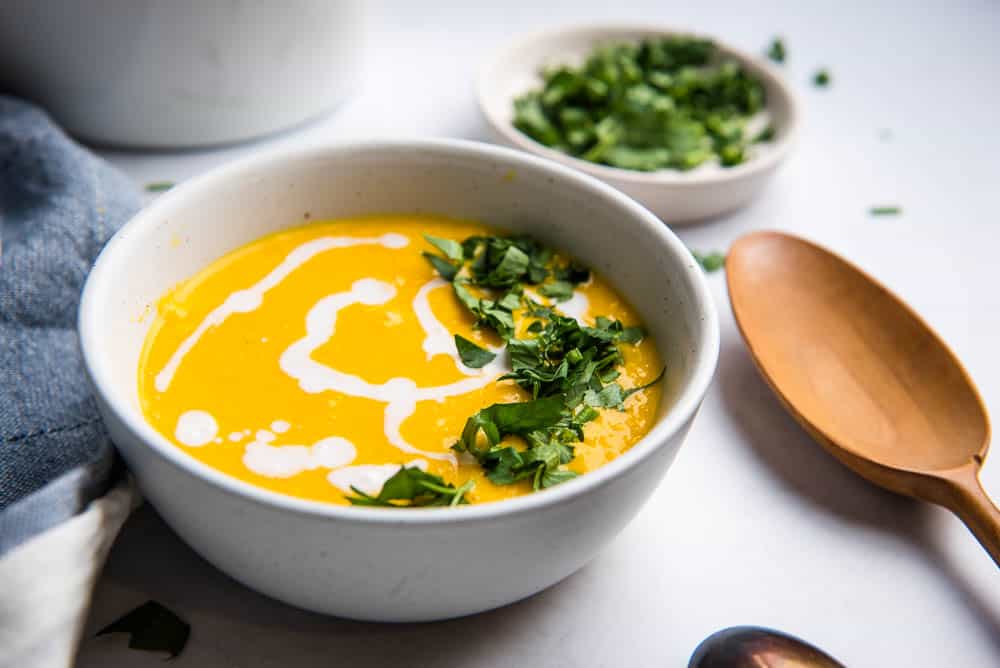 closeup of carrot ginger soup in a bowl topped with coconut milk and parsley