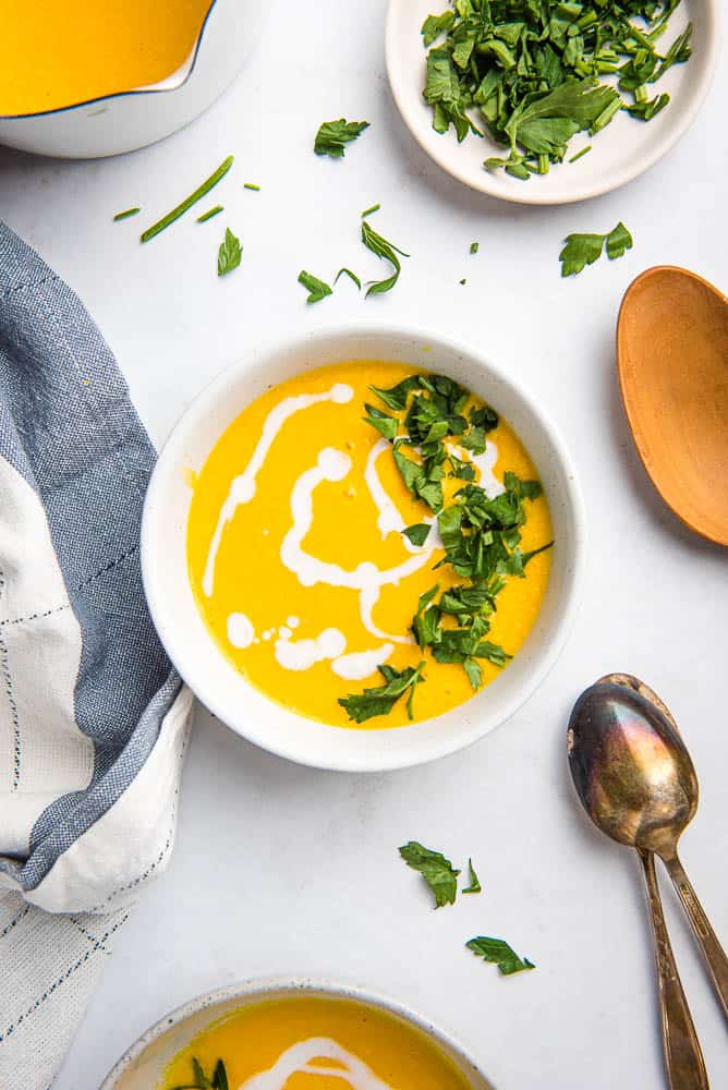 carrot ginger soup in a bowl topped with coconut milk and parsley