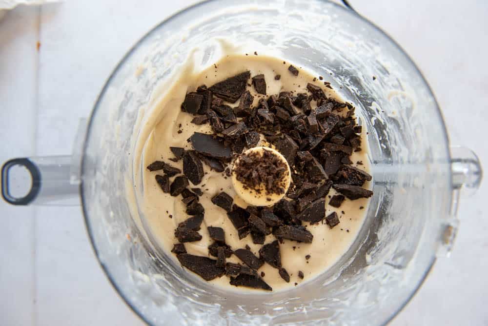 An overhead view of a blender jug with the ingredients for AIP Chocolate Chip Ice Cream poured into it.