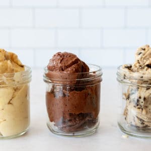 A side view of three single-portion sized mason jars, filled with scoops of AIP Ice Cream. Each jar contains a single flavor; on the right is a jar of Chocolate Chip Ice Cream, in the middle a jar of Cherry Chocolate Ice Cream and at the left a jar of Pina Colada Ice Cream. The picture is square sized and the two outer jars are cut in half.